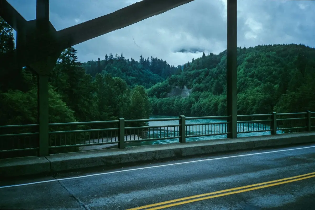 Brücke über einen grünen Fluss zwischen bewaldeten Bergen, tiefe Regenwolken