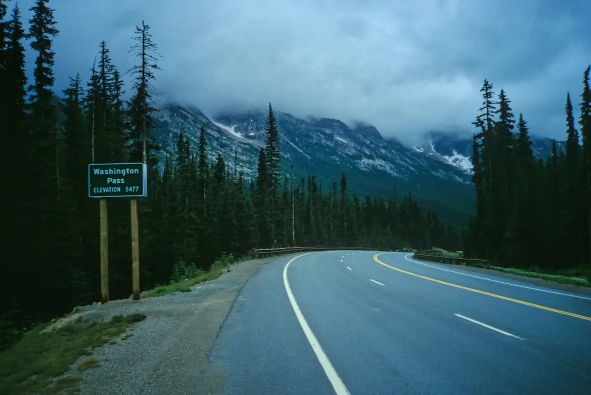 Passschild Washington Pass an der nassen Straße, dahinter Berge in Wolken