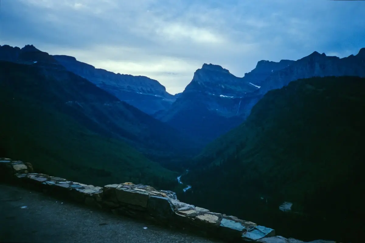 Dunkles Hochgebirgstal im Glacier National Park in der Dämmerung, im Vordergrund eine Steinmauer