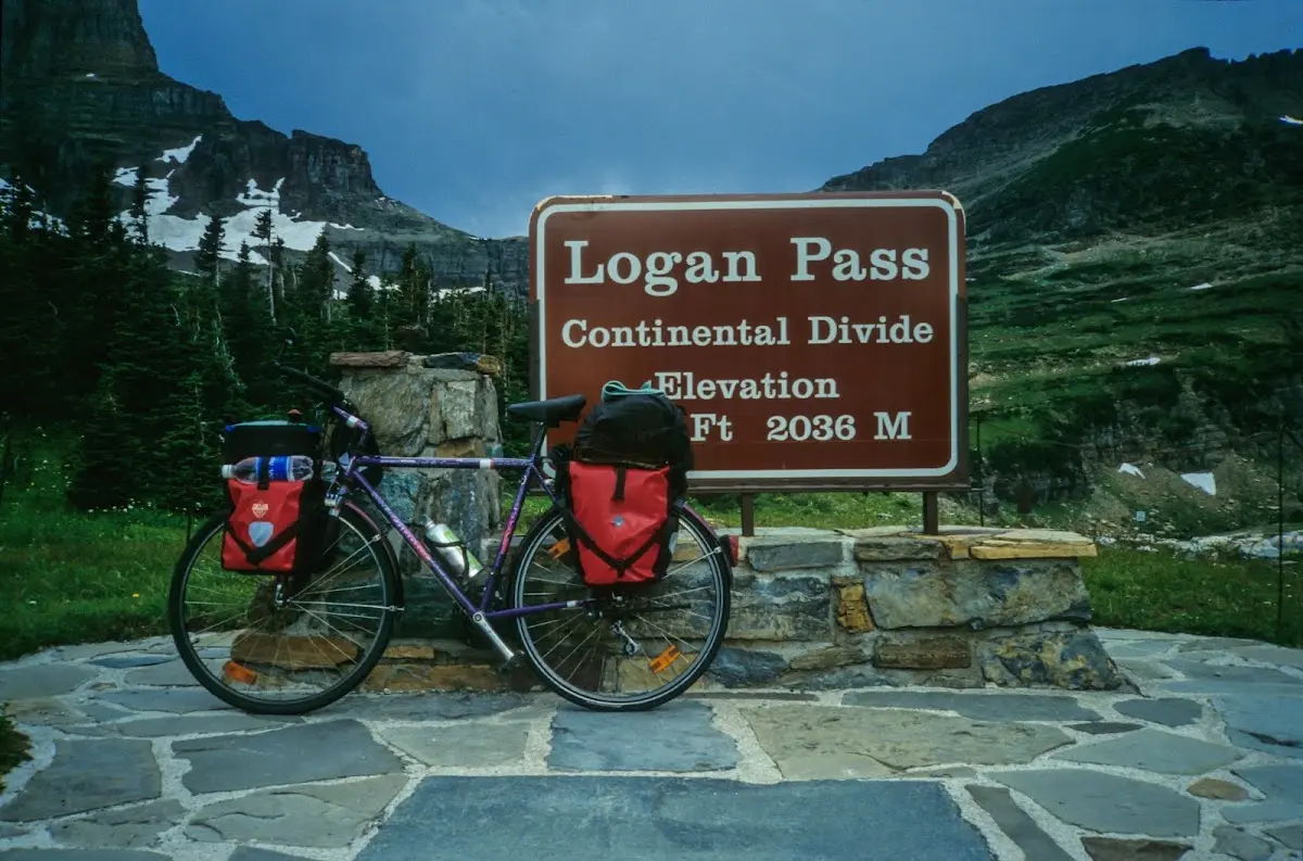 Reiserad mit roten Packtaschen vor dem Schild Logan Pass, Continental Divide, 2036 m