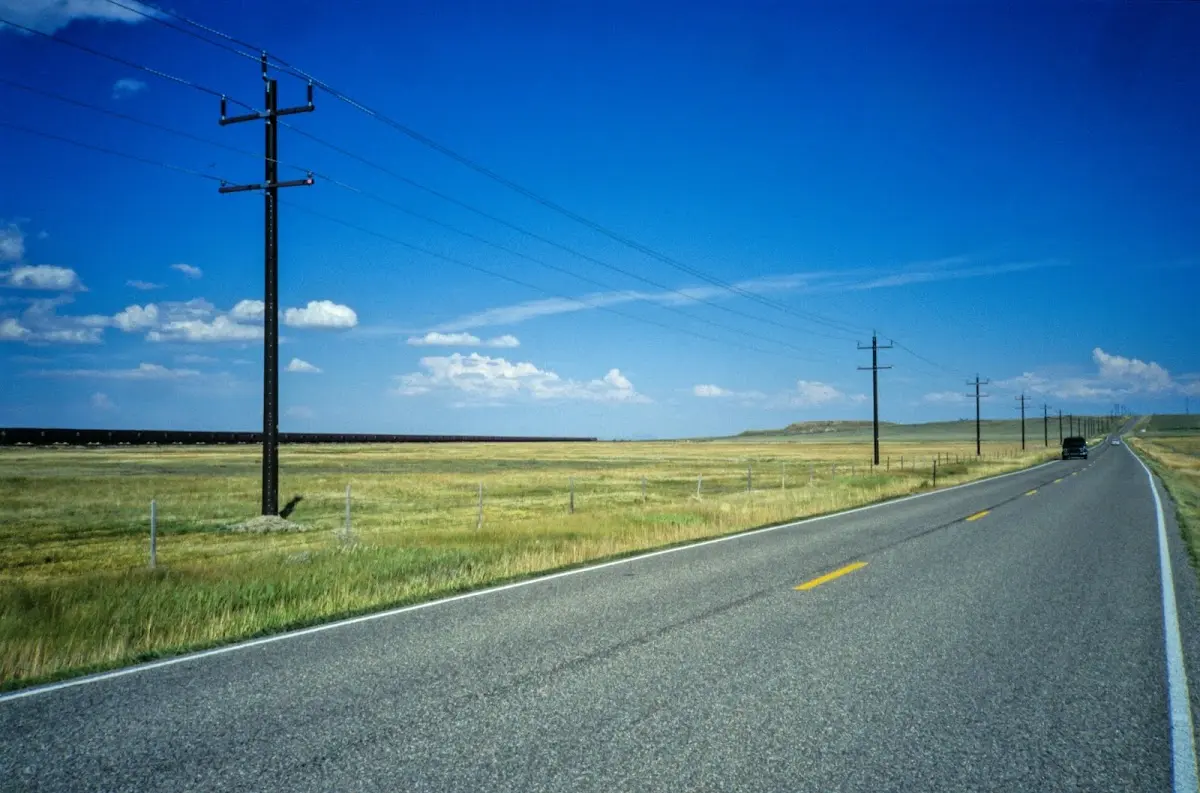 Gerade Straße durch gelbes Grasland mit Telegrafenmasten unter blauem Himmel
