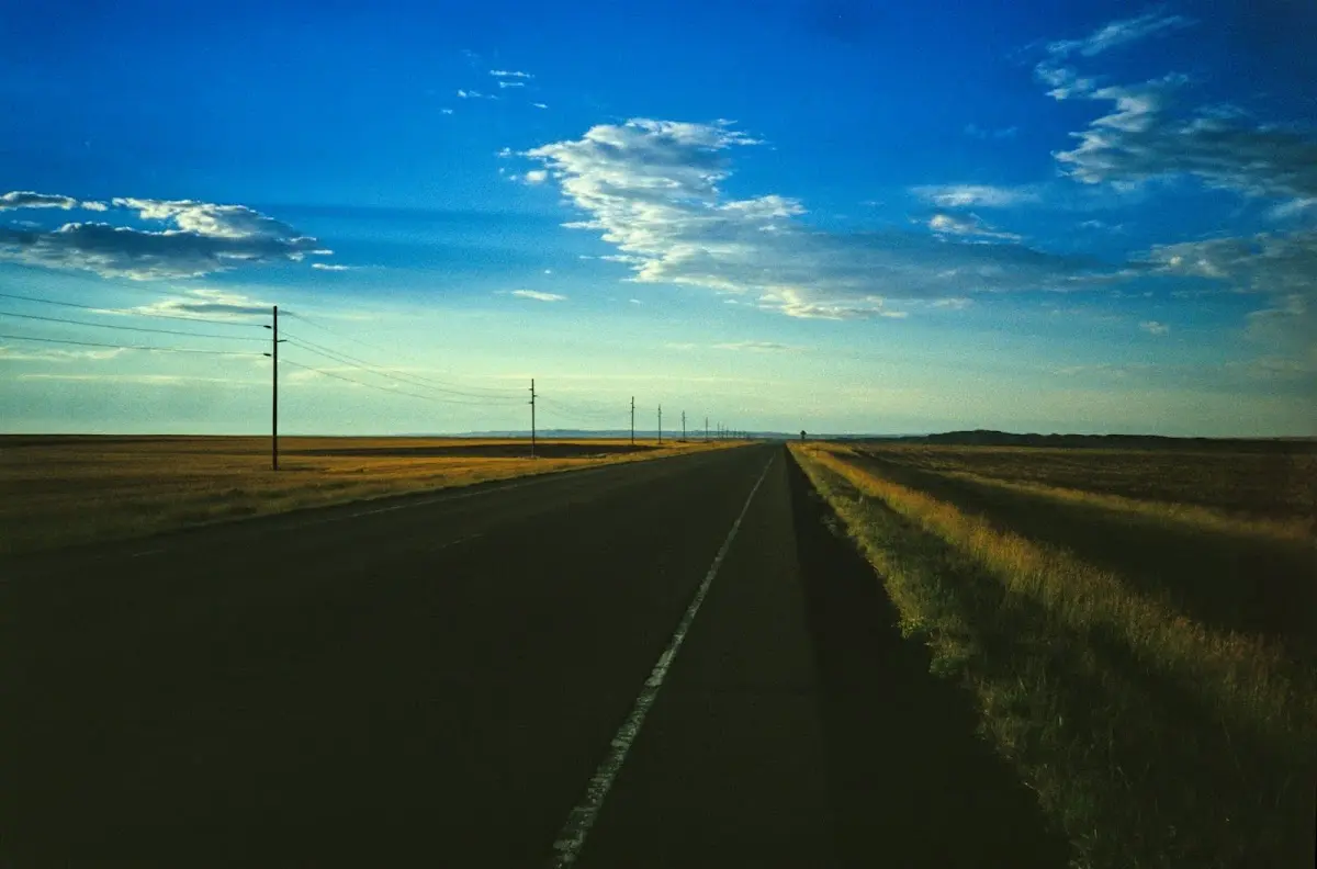Schnurgerade Straße durch die weite Prärie unter blauem Himmel mit Wolken