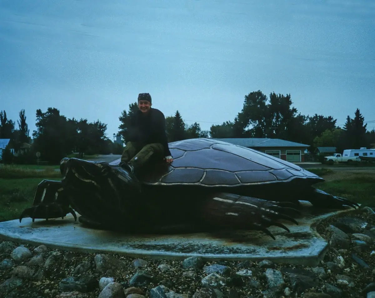 Riesige Schildkröten-Skulptur in Turtle Lake, darauf sitzt ein Mann