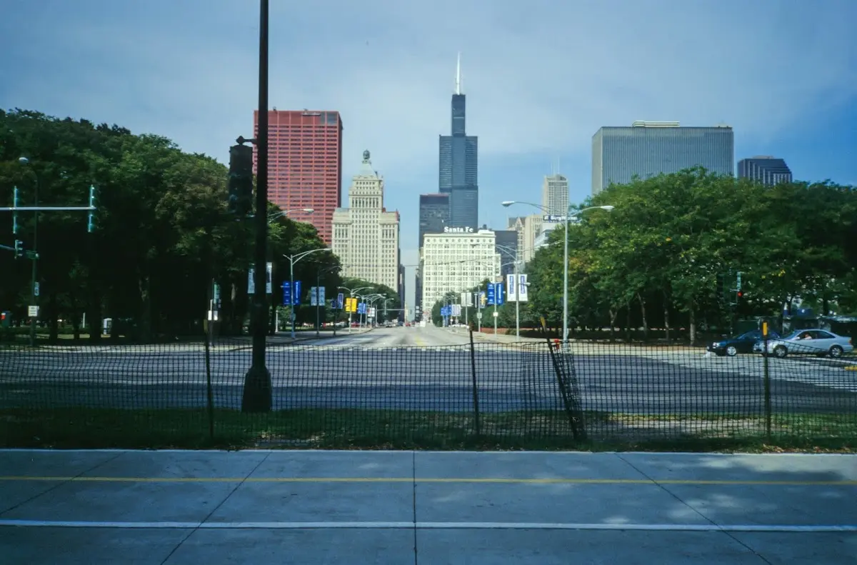 Blick durch einen Zaun auf eine Straße, an deren Ende der Willis Tower aufragt
