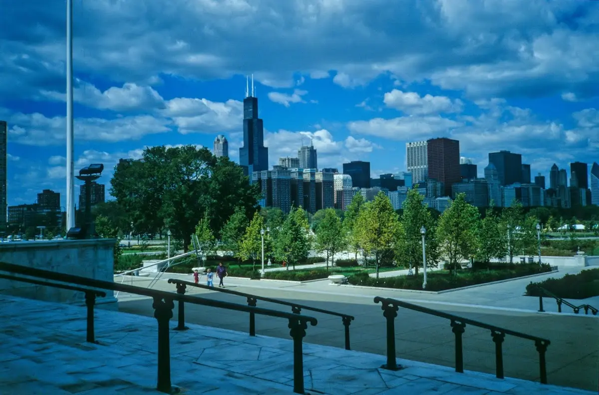 Skyline von Chicago mit dem Willis Tower über einem Park, im Vordergrund ein Treppengeländer