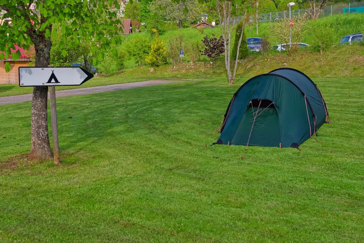 Zelt auf einer Campingwiese neben einem Zeltplatz-Schild