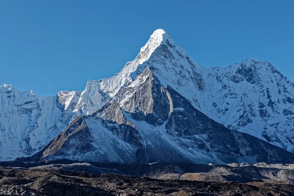 Ama Dablam, a sharp snow-covered peak, rising above a dark moraine under a deep blue sky